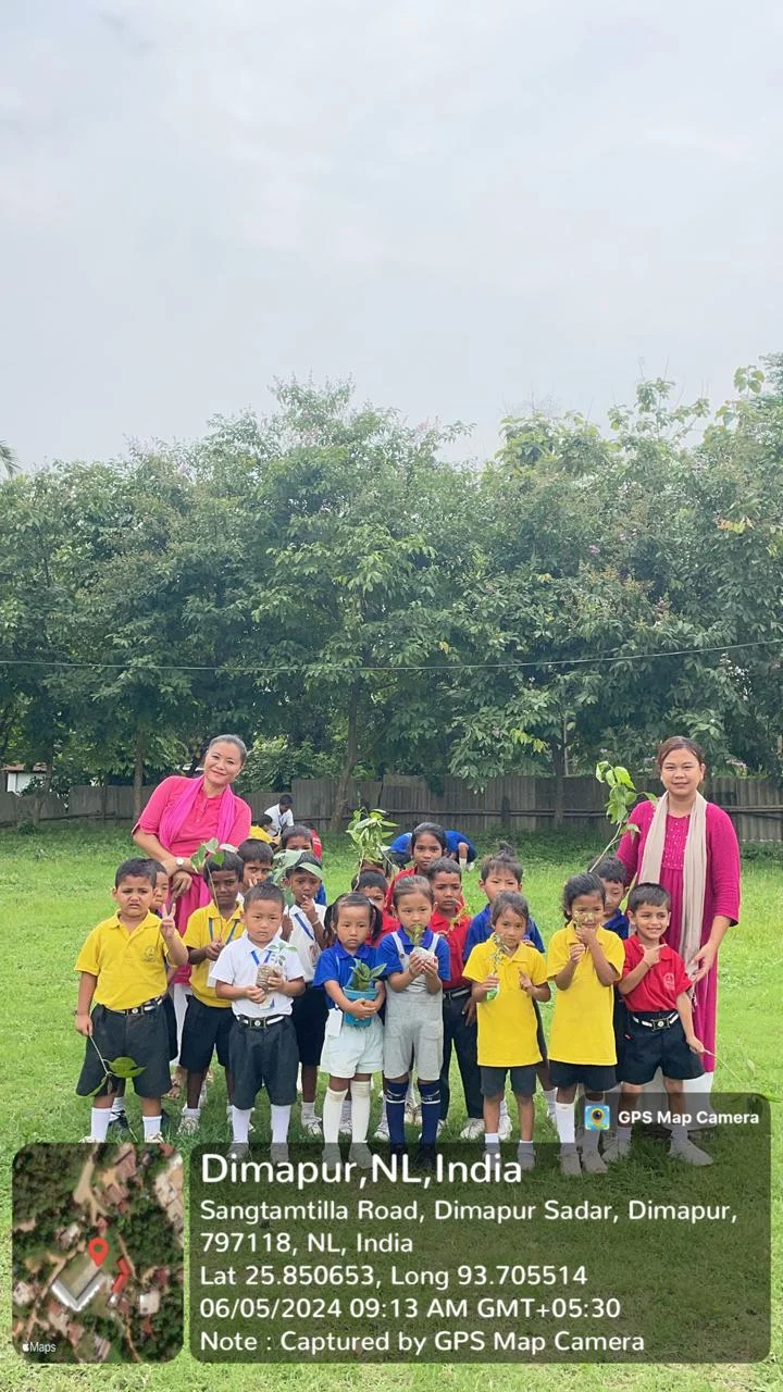 Young children and teachers holding saplings on the school grounds